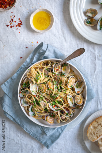 Top down view of pasta vongole, linguini with clams red pepper flakes and olive oil on white background with blue napkin