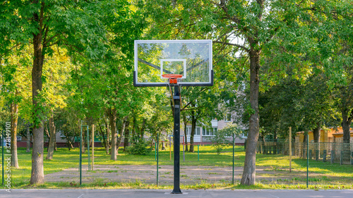 backboard on metal pole on basketball playground in city park with greenery