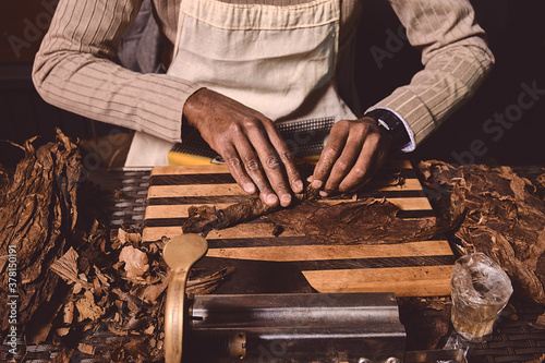 Process of making traditional cigars from tobacco leaves with hands using a mechanical device and press. Leaves of tobacco for making cigars. Close up of men's hands making cigars. © Dmitry Yakovtsev