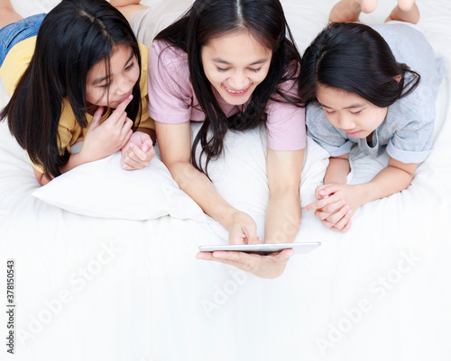 Top view Happy Asian family enjoy and relax on bed in bedroom. mother and daughters enjoy using tablet together on bed.  Family concept. photo