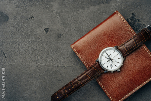 Male watch and leather wallet on dark grey surface