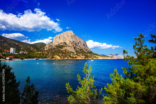 Sea landscape in Crimea. Clear blue water in nice bay, big rock, green trees. Black sea