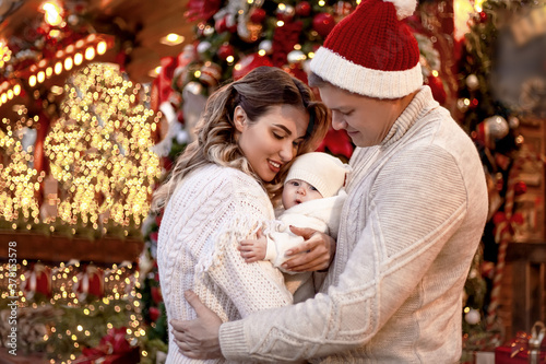 Happy family together, mother and fother holding the baby outdoor and waiting the christmas. People posing against the lights in the eve