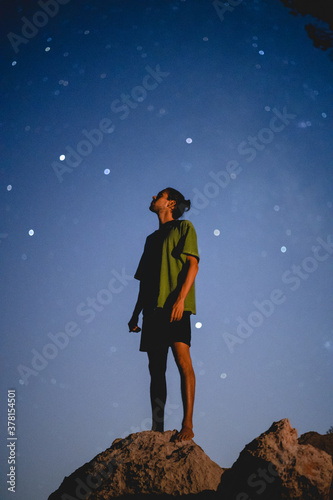 Young spanish man wearing a green shirt standing on the rocks while watching the stars in Mallorca (Spain)