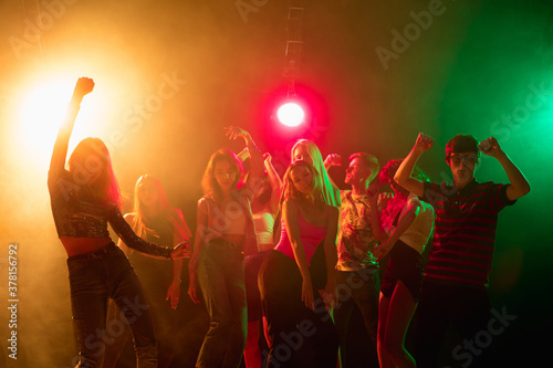 Shadows. A crowd of people in silhouette raises their hands, dancing on dancefloor on neon light background. Night life, club, music, dance, motion, youth. Bright colors and moving girls and boys.