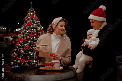 Happy family together, mother and fother holding the baby outdoor and waiting the christmas. People posing against the lights in the eve and drinking hot drinks photo