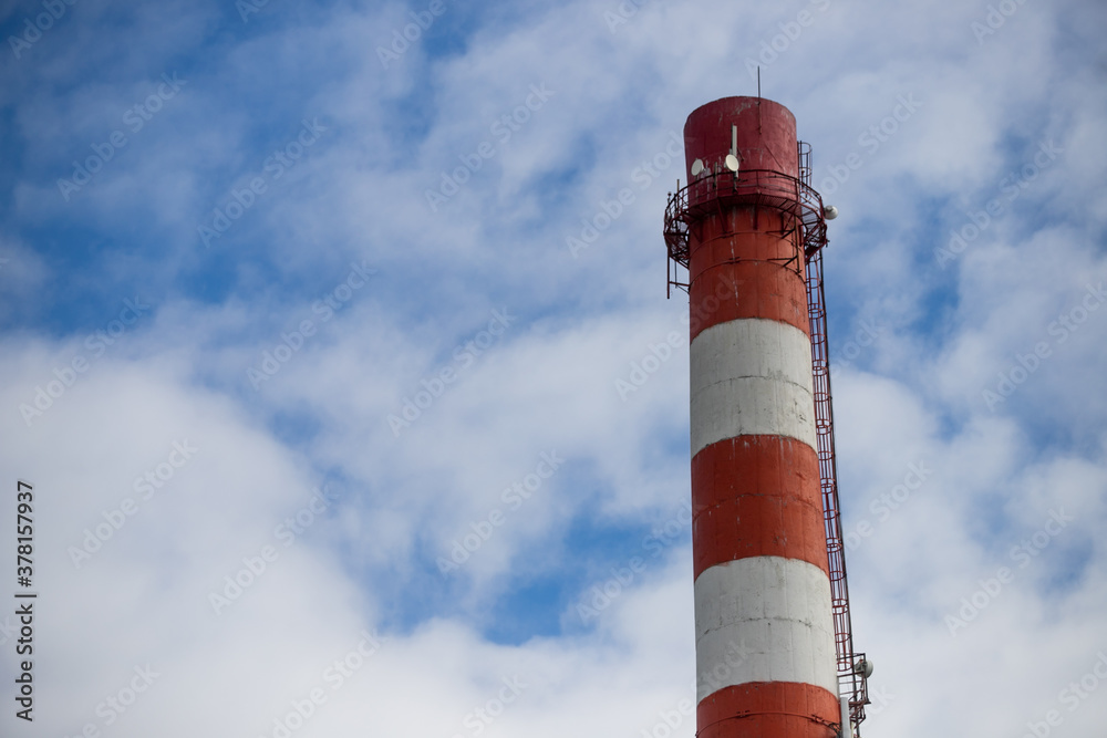 Close up of a smokeless chimney smokestack in red and white stripes on a sunny day against the blu sky