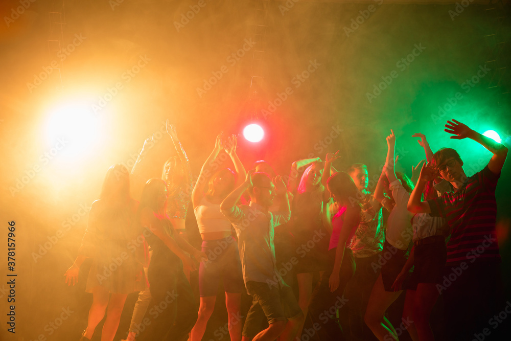 Obraz premium Carefree. A crowd of people in silhouette raises their hands, dancing on dancefloor on neon light background. Night life, club, music, dance, motion, youth. Bright colors and moving girls and boys.