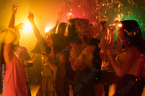 Youth. A crowd of people in silhouette raises their hands, dancing on dancefloor on neon light background. Night life, club, music, dance, motion, youth. Bright colors and moving girls and boys.