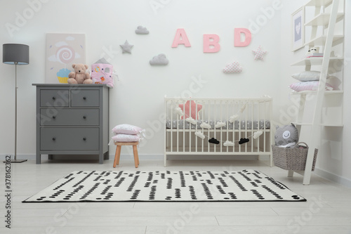 Cute baby room interior with crib and chest of drawers near white wall © New Africa