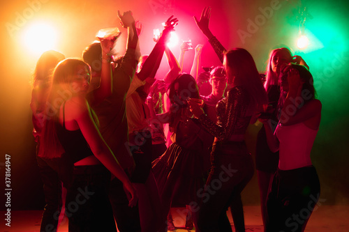Energy. A crowd of people in silhouette raises their hands, dancing on dancefloor on neon light background. Night life, club, music, dance, motion, youth. Bright colors and moving girls and boys.