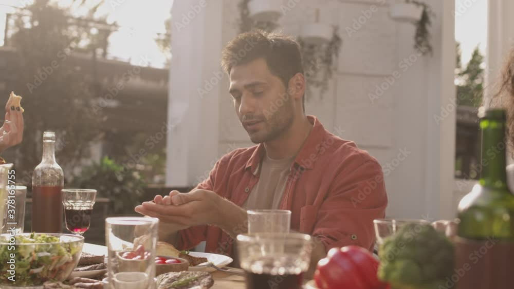 Panning of several multiethnic young men and women are sitting at cafe table, having dinner and communicating Panning of several multiethnic young men and women are sitting at cafe table, having dinner and communicating