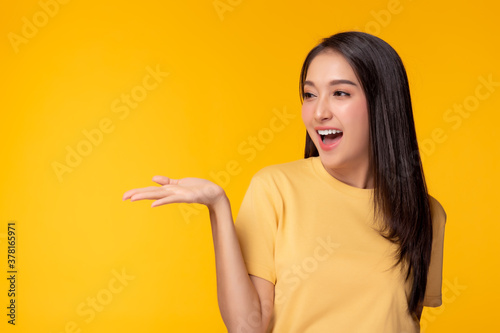 Obraz na plátně Happy beautiful young asian woman with yellow background holding copy space imaginary on beauty palm for insert advertisement, happiness and smiley face