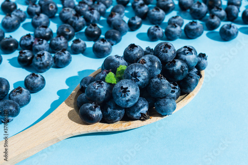 Blueberries in a wooden spoon on blue background. Closeup organic raw vegan dessert food.