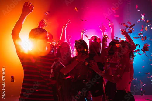 Juice. A crowd of people in silhouette raises their hands, dancing on dancefloor on neon light background. Night life, club, music, dance, motion, youth. Bright colors and moving girls and boys.