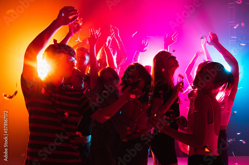 Festive. A crowd of people in silhouette raises their hands, dancing on dancefloor on neon light background. Night life, club, music, dance, motion, youth. Bright colors and moving girls and boys.