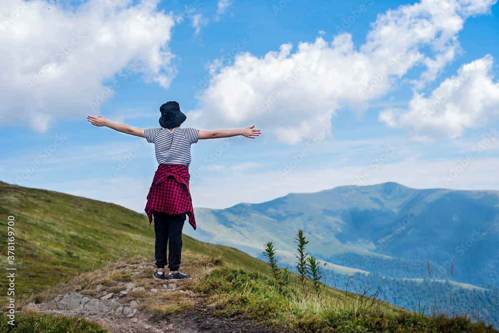 In the beautiful summer mountains, a young girl raised her hands and enjoys the strength and freedom of the mountains. Teen girl facing the mountains