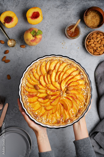 Female hands holding ceramic dish with fruit tart. Peach cakes with almonds. Homemade dessert. Top view, food concrete background
