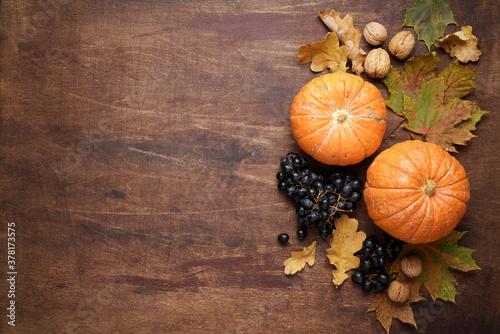 Festive autumn décor on wooden brown background. Pumpkins, walnuts, grapes and fallen leaves. Concept of Thanksgiving day or Halloween. Flat lay autumn composition with copy space