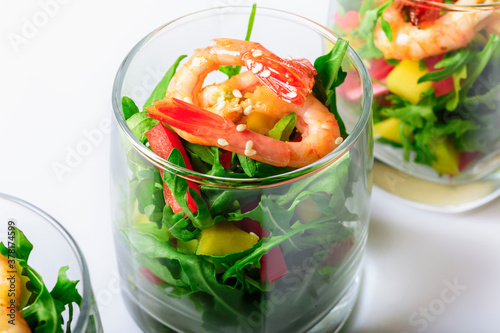A salad of mango, sweet pepper, rukkola and garlic-fried shrimp in a glass. Close up. Selective focus. White background.