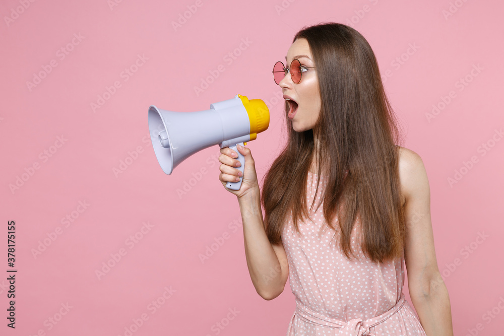 Shocked excited amazed young brunette woman 20s wearing pink summer dotted dress eyeglasses posing screaming in megaphone looking aside isolated on pastel pink color wall background studio portrait. Shocked excited amazed young brunette woman 20s wearing pink summer dotted dress eyeglasses posing screaming in megaphone looking aside isolated on pastel pink color wall background studio portrait.