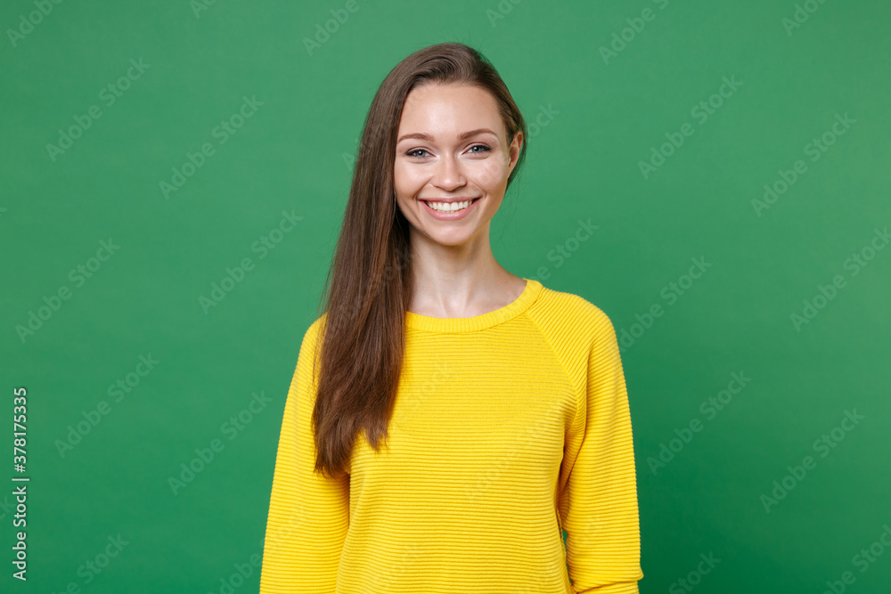 Smiling beautiful attractive charming pretty funny young brunette woman 20s wearing yellow casual clothes posing standing and looking camera isolated on green color wall background, studio portrait. Smiling beautiful attractive charming pretty funny young brunette woman 20s wearing yellow casual clothes posing standing and looking camera isolated on green color wall background, studio portrait.