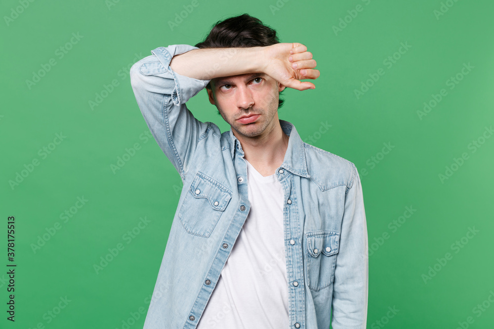 Exhausted tired displeased young brunet man 20s wearing casual clothes white t-shirt denim shirt posing standing put hand on head looking aside isolated on green color wall background studio portrait. Exhausted tired displeased young brunet man 20s wearing casual clothes white t-shirt denim shirt posing standing put hand on head looking aside isolated on green color wall background studio portrait.