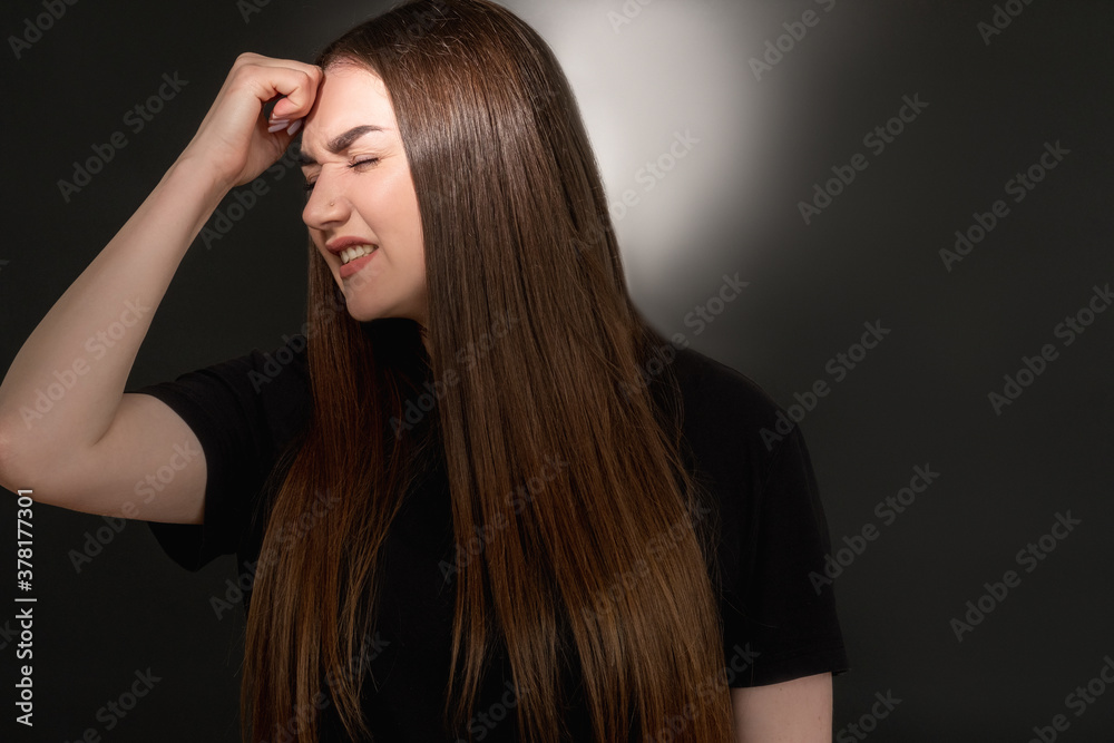 Obraz premium Hurt woman portrait. Domestic violence. Frustrated overweight lady in black t-shirt suffering from headache with closed eyes isolated on dark illuminated copy space background.
