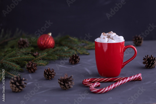 red Cup with coffee and marshmallows, Christmas candy folded in the form of a heart, a ball, cones and branches of a fir tree on a black background