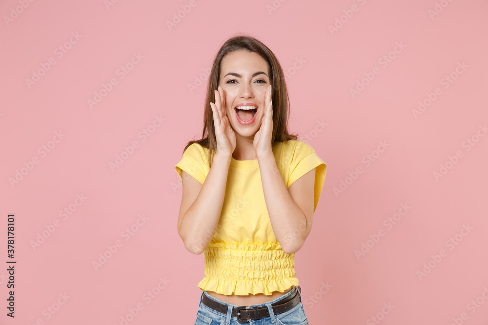 Cheerful young brunette woman 20s wearing yellow casual t-shirt posing standing screaming with hands gesture near mouth looking camera isolated on pastel pink color wall background studio portrait. Cheerful young brunette woman 20s wearing yellow casual t-shirt posing standing screaming with hands gesture near mouth looking camera isolated on pastel pink color wall background studio portrait.