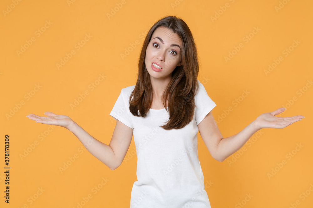 Perplexed puzzled confused young brunette woman 20s wearing white blank empty design casual t-shirt posing standing spreading hands looking camera isolated on yellow color background studio portrait. Perplexed puzzled confused young brunette woman 20s wearing white blank empty design casual t-shirt posing standing spreading hands looking camera isolated on yellow color background studio portrait.