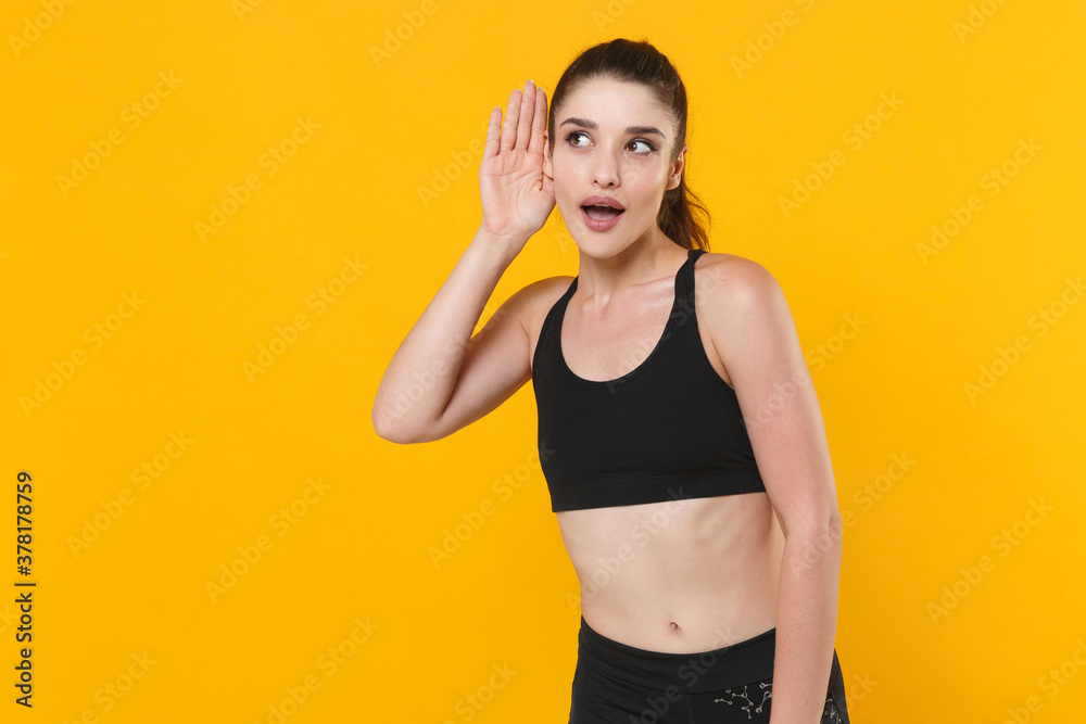 Shocked curious young fitness sporty woman 20s wearing black sportswear posing training try to hear you overhear listening intently looking aside isolated on yellow color background studio portrait. Shocked curious young fitness sporty woman 20s wearing black sportswear posing training try to hear you overhear listening intently looking aside isolated on yellow color background studio portrait.