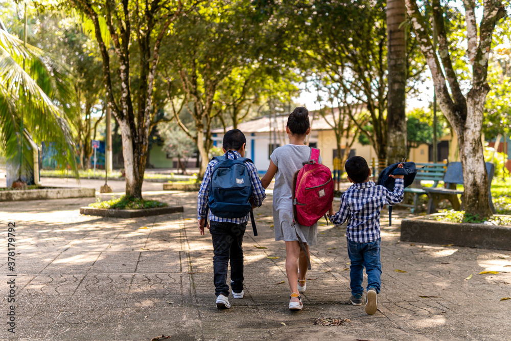 Fototapeta premium three children walking hand in hand in a park with school bag