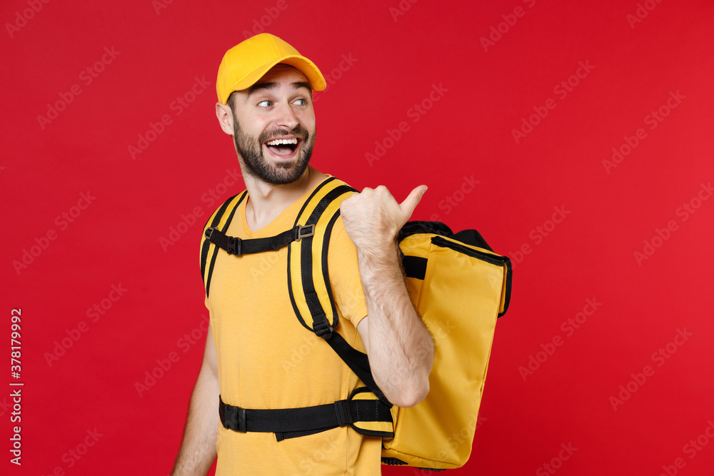 Delivery man 20s in yellow cap t shirt uniform thermal bag backpack points finger aside isolated on red background studio Guy male employee work as courier Service coronavirus covid-19 virus concept Delivery man 20s in yellow cap t shirt uniform thermal bag backpack points finger aside isolated on red background studio Guy male employee work as courier Service coronavirus covid-19 virus concept