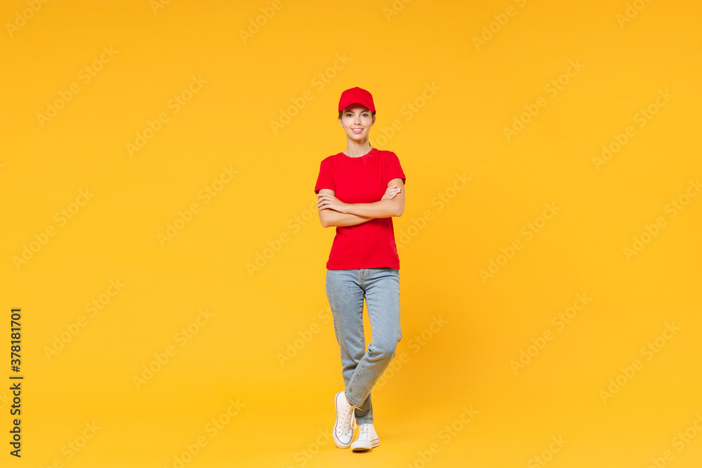Full length body delivery employee woman in red cap blank t-shirt uniform work courier in service during quarantine coronavirus covid-19 virus standing isolated on yellow background studio portrait.