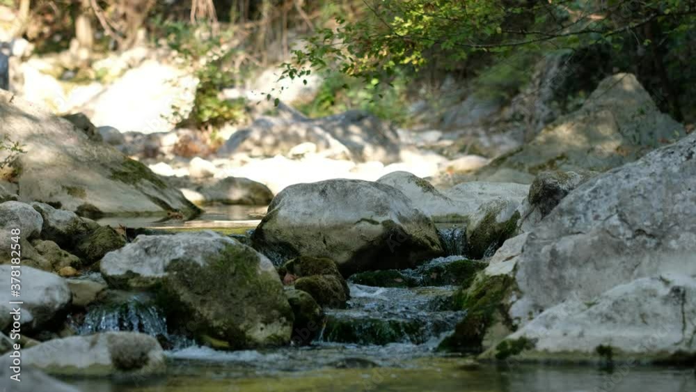 Small river enveloped with rocks and the rocks reflected in the calm water surface streaming in the middle of forest. Calm mysterious streaming river in the middle of forest. Small river enveloped with rocks and the rocks reflected in the calm water surface streaming in the middle of forest. Calm mysterious streaming river in the middle of forest.