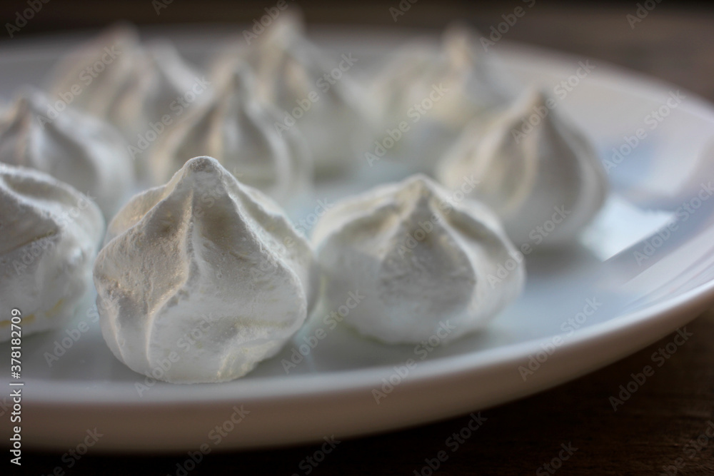 Close-up of meringue on a white plate. Marshmallows on wooden table background Close-up of meringue on a white plate. Marshmallows on wooden table background