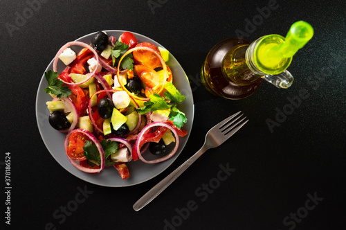 Plate with Greek salad and fork. Greek salad and dark background. Bottle of olive oil.