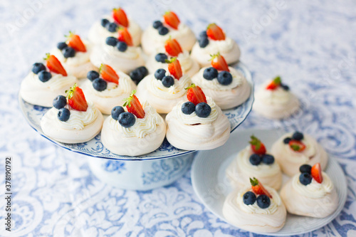 Homemade meringue Pavlova cakes with fresh berries: strawberry and blueberry on white platter on light blue tablecloth