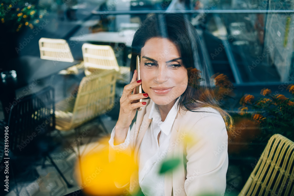 Beautiful caucasian woman making mobile phone call satisfied with connections and tariffs sitting at cafe, positive female millennial using smartphone for making call to banking service operator