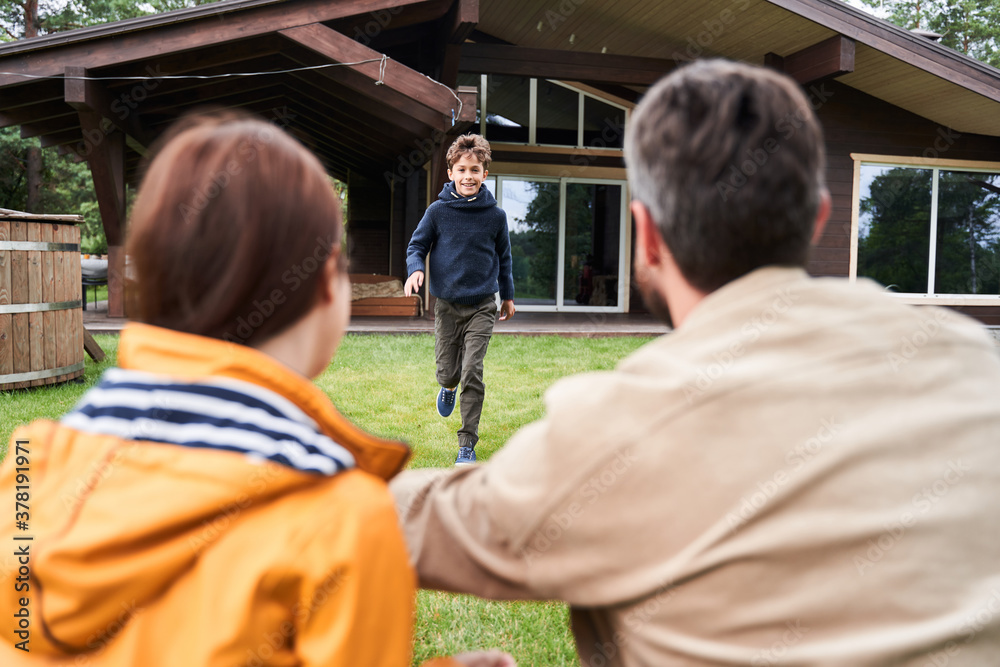 Fototapeta premium Cheerful adorable boy running to parents outdoors