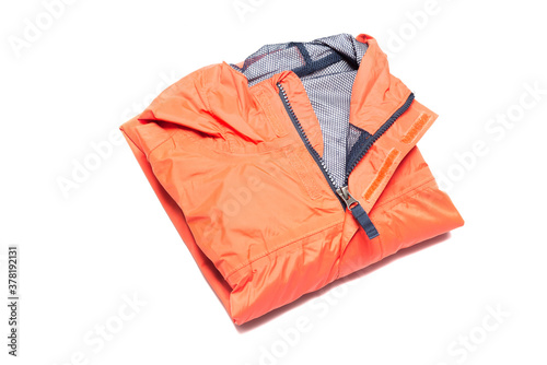 Folded orange zipper windbreaker jacket, rain proof and waterproof hiking Gore-Tex jacket hoodie. Track jacket sport nylon full zip isolated on white. Folded clothes. Outer layer garment for travel.