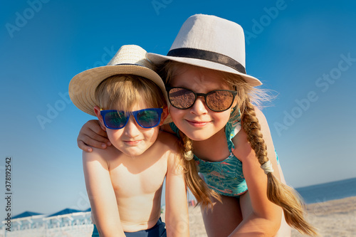 Sibling on beach. Children at sea on summer family vacation. Kids in sunglasses and sunhat. Brother and sister look at me on the photo.