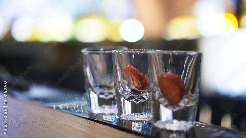 Three shot glasses on bar counter with garnish, on background of bokeh lights. Close up shot of glasses on background of bokeh lights, small shot glasses on table in bar Three shot glasses on bar counter with garnish, on background of bokeh lights. Close up shot of glasses on background of bokeh lights, small shot glasses on table in bar