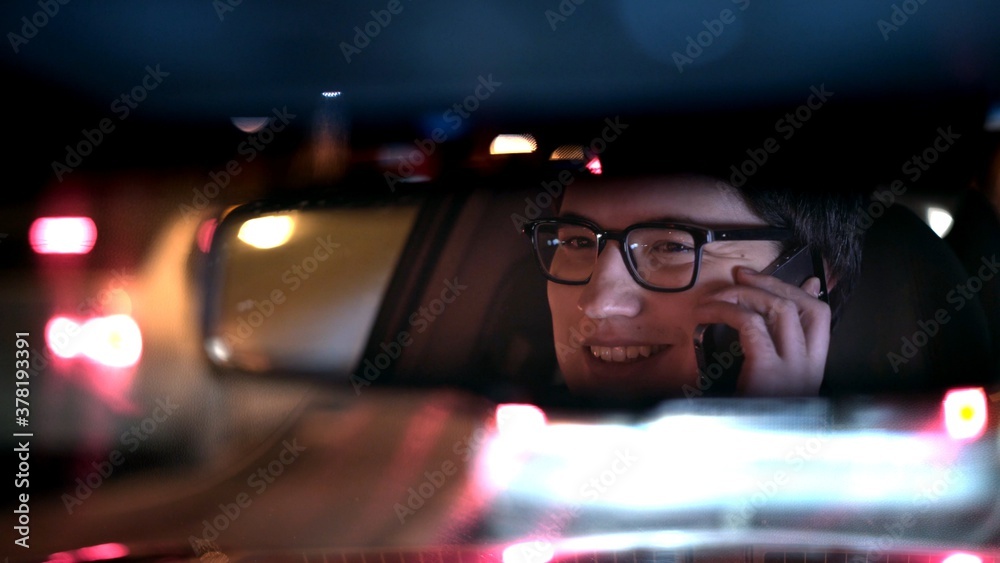 Driver talking on the phone, reflected in a rear view mirror, night shot. Driver in a mirror in car, night call on the road shot driving all night from backseat Driver talking on the phone, reflected in a rear view mirror, night shot. Driver in a mirror in car, night call on the road shot driving all night from backseat