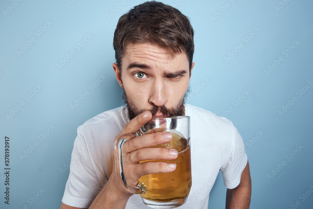 Cheerful man in a white T-shirt with a beer mug drunk blue background Cheerful man in a white T-shirt with a beer mug drunk blue background