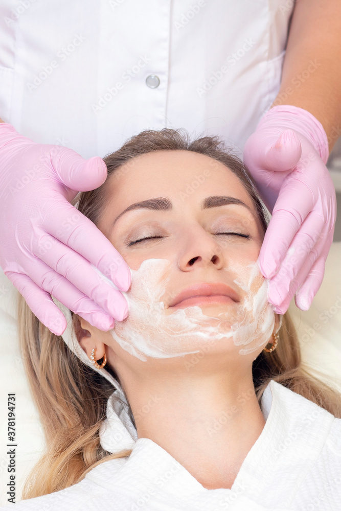cosmetology. Close up picture of lovely young woman with closed eyes receiving facial cleansing procedure in beauty salon. VERTICAL PHOTO