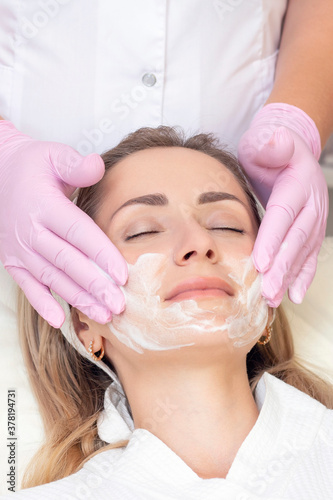 cosmetology. Close up picture of lovely young woman with closed eyes receiving facial cleansing procedure in beauty salon. VERTICAL PHOTO