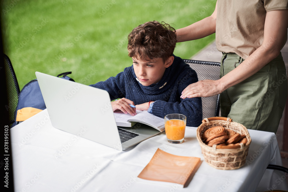 Adorable boy using laptop while studying with mother outdoors