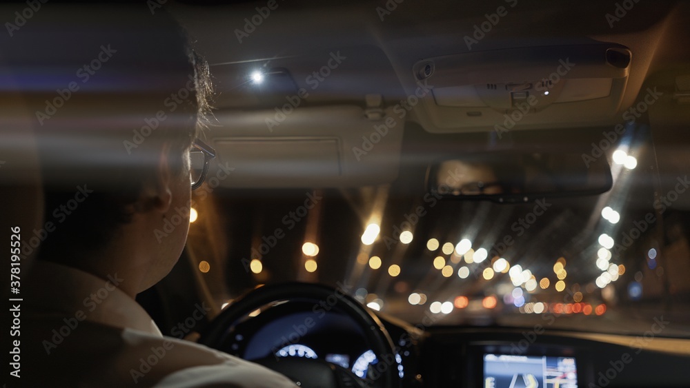 View from back seat of car at night, male driver in eyeglasses back. Night city shot, bokeh lights on the road, taxi driver. Lens flare View from back seat of car at night, male driver in eyeglasses back. Night city shot, bokeh lights on the road, taxi driver. Lens flare